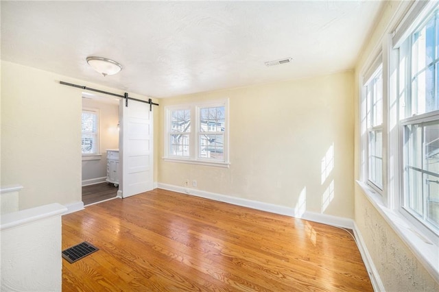 unfurnished bedroom featuring baseboards, a barn door, visible vents, and wood finished floors