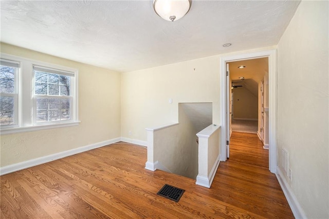 corridor with baseboards, visible vents, an upstairs landing, and wood finished floors