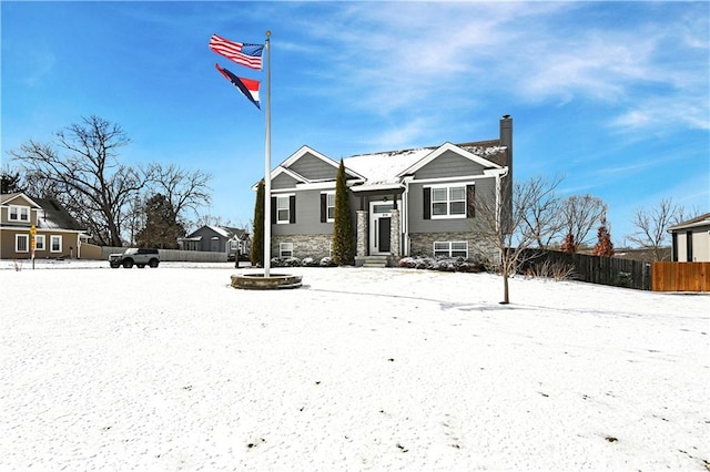 view of front facade featuring stone siding, fence, and a chimney