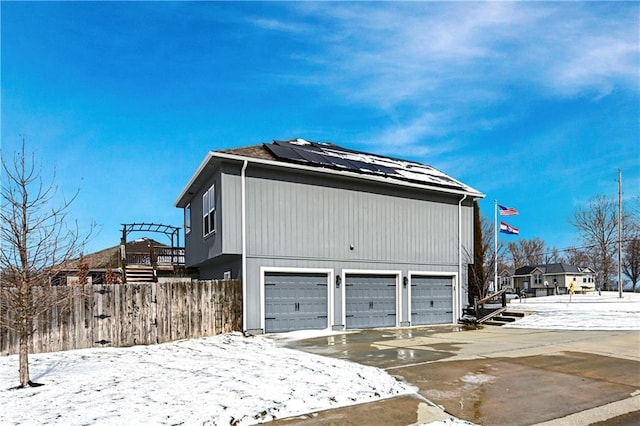 view of snowy exterior featuring a garage, fence, and solar panels