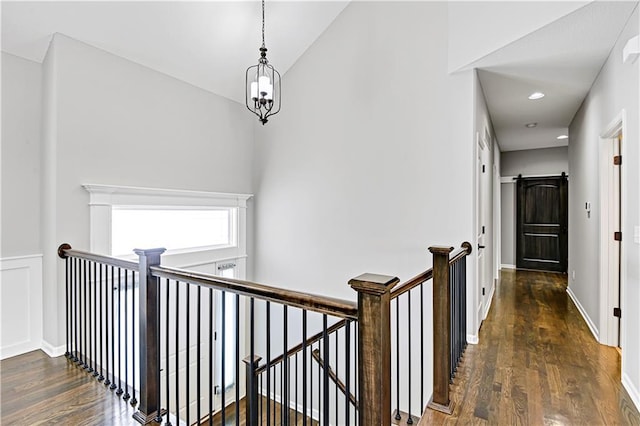 corridor with wood finished floors, baseboards, an upstairs landing, and a barn door