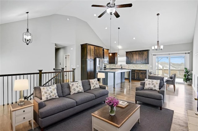 living area featuring light wood-style floors, high vaulted ceiling, and ceiling fan with notable chandelier