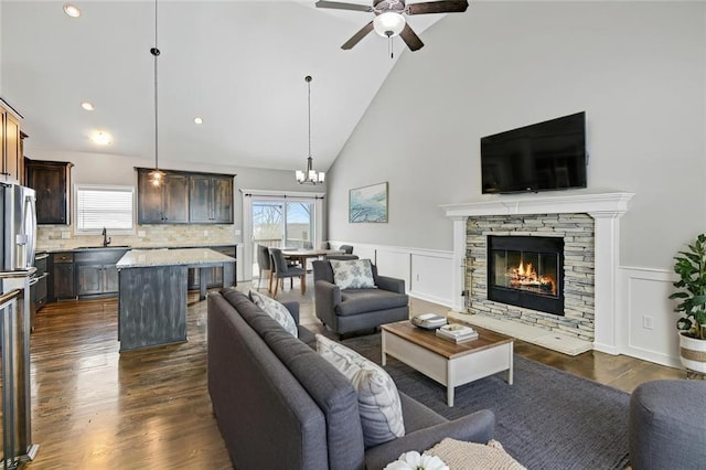 living area featuring dark wood-style floors, a wainscoted wall, a fireplace, and ceiling fan with notable chandelier