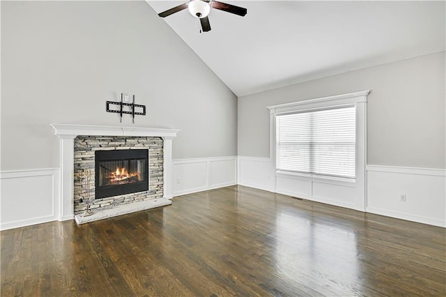 unfurnished living room featuring a stone fireplace, a wainscoted wall, wood finished floors, visible vents, and a ceiling fan