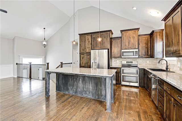 kitchen featuring appliances with stainless steel finishes, dark wood-style flooring, a center island, light stone countertops, and a sink