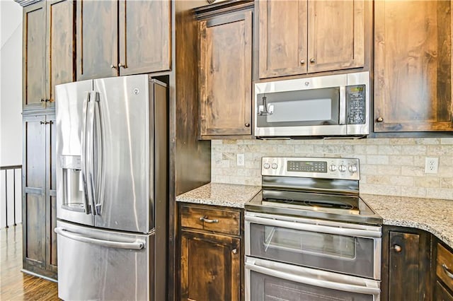 kitchen with wood finished floors, dark brown cabinets, appliances with stainless steel finishes, light stone countertops, and tasteful backsplash