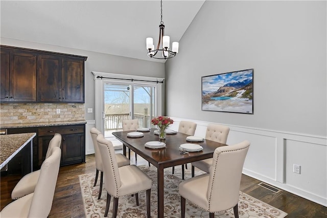 dining space featuring visible vents, wainscoting, dark wood-type flooring, vaulted ceiling, and a notable chandelier