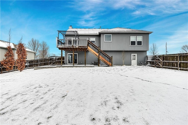 snow covered house featuring a deck, a chimney, a fenced backyard, and stairway