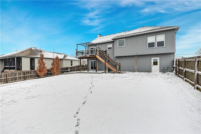 snow covered rear of property with a deck, stairway, and a fenced backyard