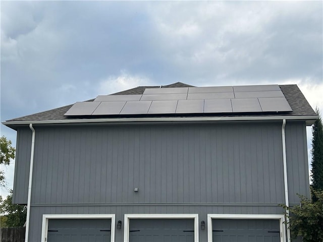 view of property exterior with a garage, a shingled roof, and roof mounted solar panels