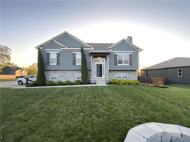 raised ranch with stone siding, fence, a chimney, and a front lawn