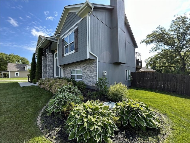 view of property exterior with stone siding, a lawn, a chimney, and fence