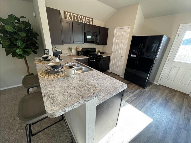 kitchen with a breakfast bar area, wood finished floors, a peninsula, vaulted ceiling, and black appliances