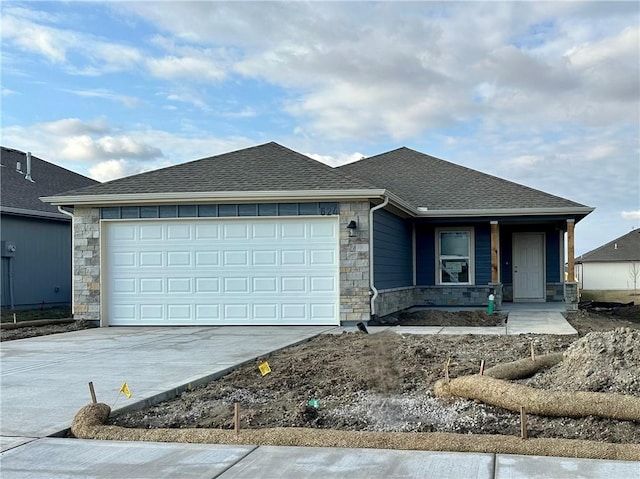 view of front of house with a shingled roof, stone siding, concrete driveway, and a garage