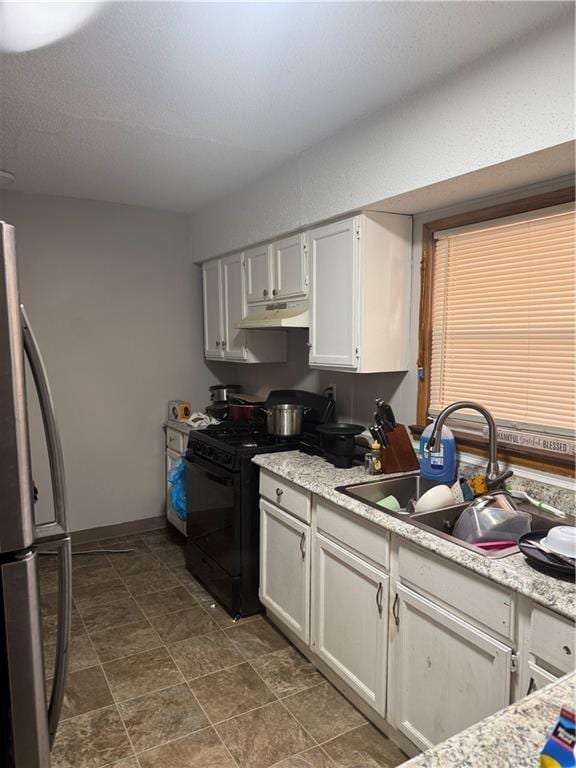 kitchen featuring under cabinet range hood, black gas range, light countertops, freestanding refrigerator, and a sink