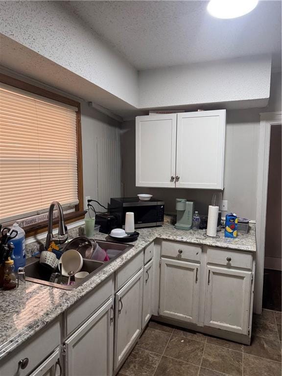 kitchen with a textured ceiling, stainless steel microwave, and a sink