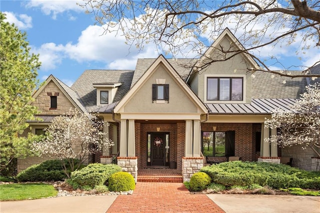 view of front of house with a standing seam roof, a porch, roof with shingles, and brick siding