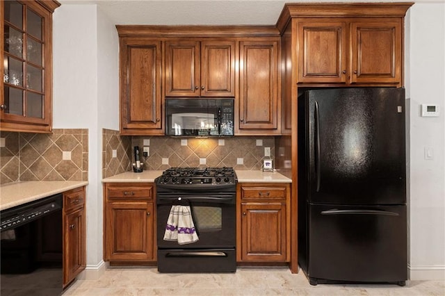 kitchen featuring light countertops, backsplash, black appliances, and glass insert cabinets