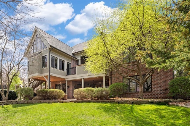 rear view of property featuring a balcony, a shingled roof, a lawn, and brick siding