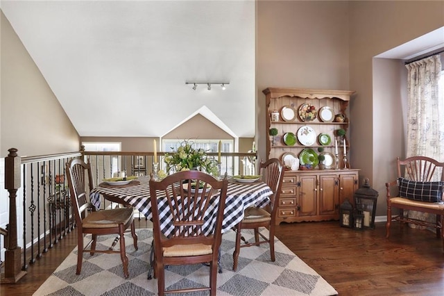 dining area featuring dark wood finished floors, track lighting, baseboards, and vaulted ceiling