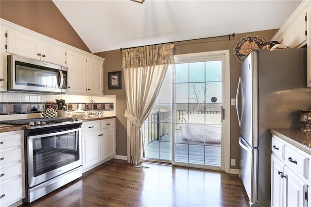 kitchen with stainless steel appliances, dark countertops, white cabinets, and vaulted ceiling