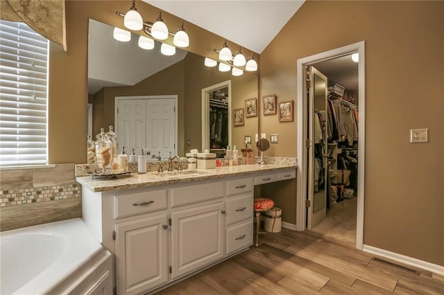 bathroom featuring vanity, wood finished floors, visible vents, lofted ceiling, and a bath