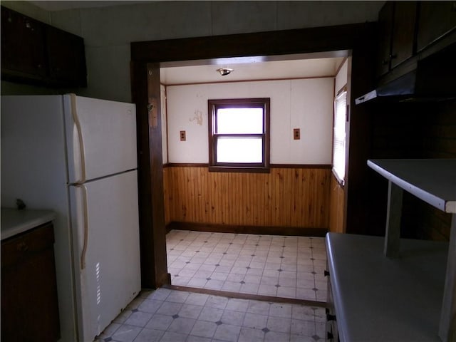 kitchen with freestanding refrigerator, a wainscoted wall, wood walls, and light floors