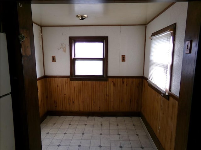 empty room featuring a wainscoted wall, crown molding, wooden walls, and light floors