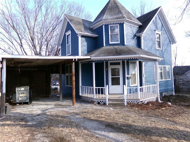 victorian-style house featuring covered porch, driveway, a carport, and a shingled roof