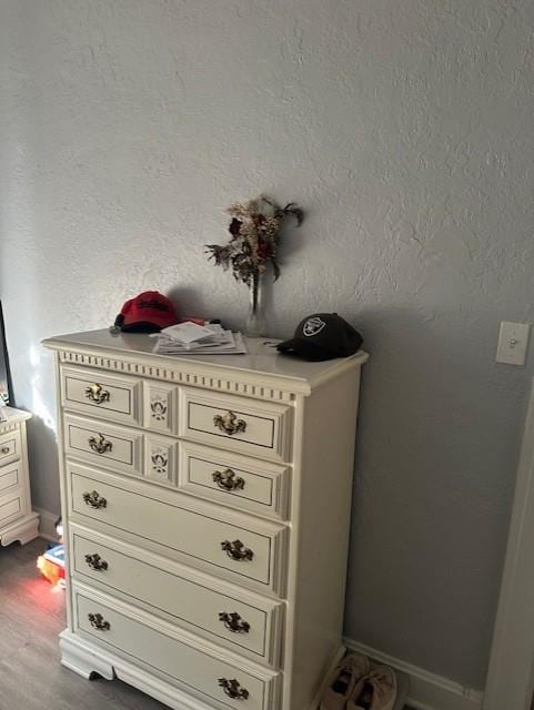 interior details featuring wood finished floors, a textured wall, and baseboards