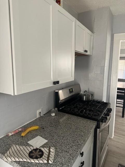 kitchen with stainless steel range with gas stovetop, light wood-type flooring, dark stone countertops, white cabinets, and a textured ceiling