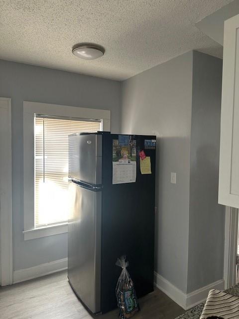 kitchen with light wood-style floors, baseboards, freestanding refrigerator, and a textured ceiling