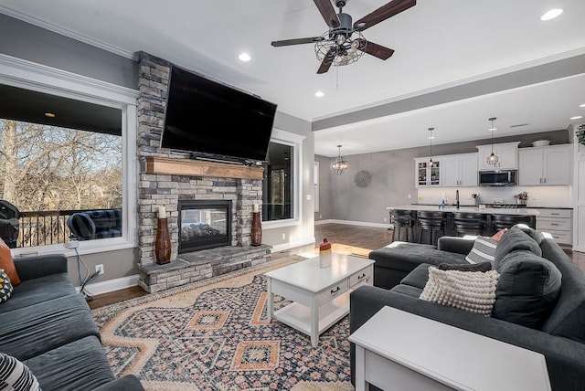 living room with baseboards, wood finished floors, a stone fireplace, and ceiling fan