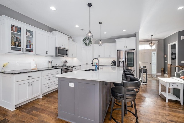 kitchen featuring a breakfast bar, an island with sink, a sink, dark wood finished floors, and stainless steel appliances