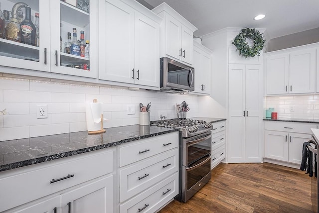 kitchen with tasteful backsplash, dark stone counters, white cabinets, stainless steel appliances, and dark wood-style flooring