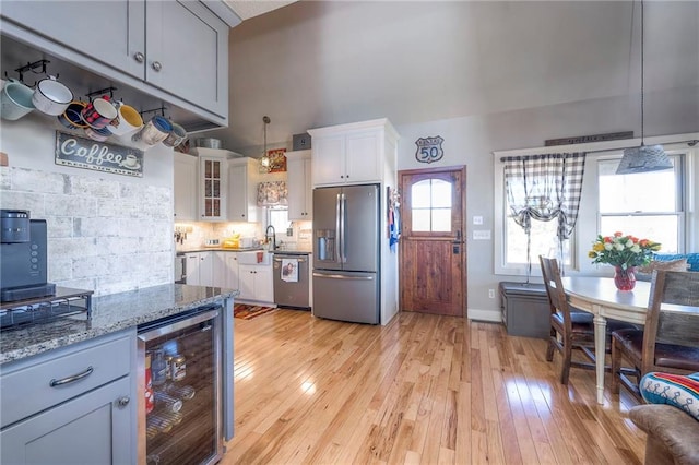 kitchen with light stone countertops, wine cooler, decorative light fixtures, light wood-type flooring, and stainless steel appliances