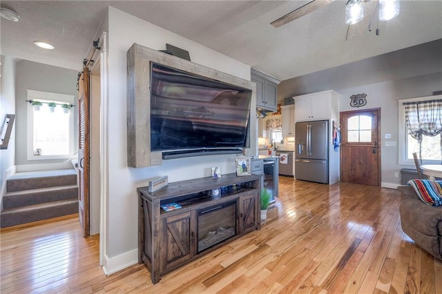 living room with baseboards, a textured ceiling, a ceiling fan, and light wood-style floors