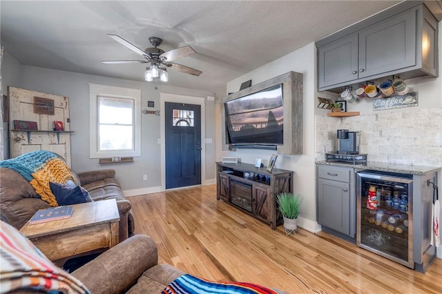 living area featuring a ceiling fan, baseboards, wine cooler, light wood-style floors, and a dry bar