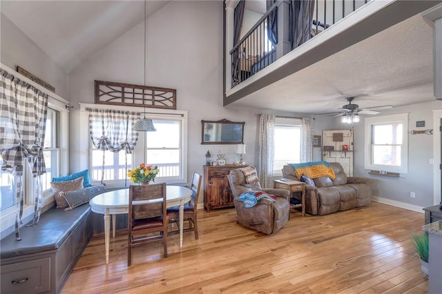 living area featuring a healthy amount of sunlight, ceiling fan with notable chandelier, light wood-type flooring, and baseboards