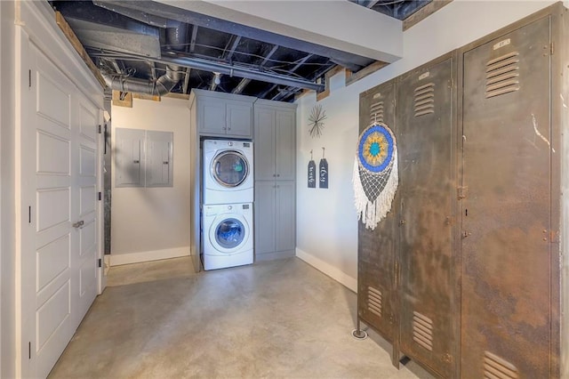 clothes washing area with electric panel, cabinet space, stacked washing maching and dryer, and baseboards