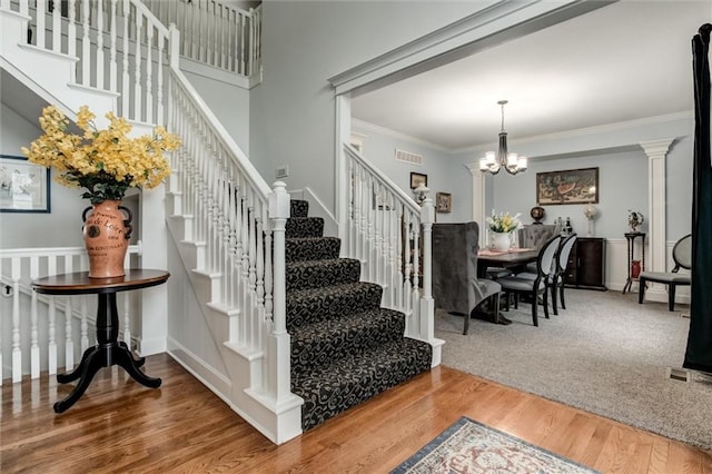 staircase with a chandelier, ornamental molding, wood finished floors, and visible vents