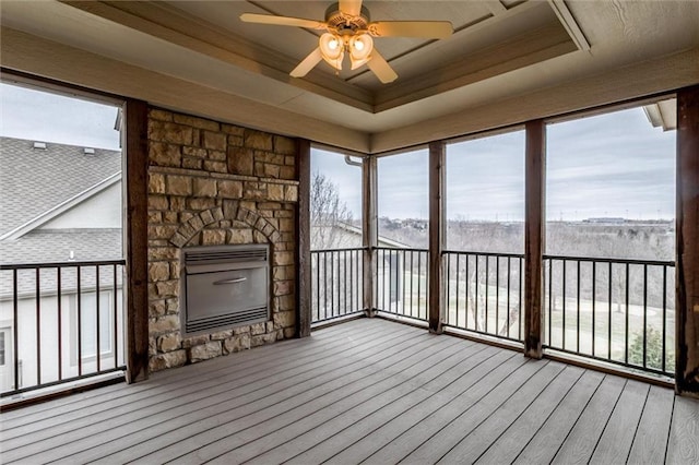 unfurnished sunroom with ceiling fan, a fireplace, a raised ceiling, and a wealth of natural light