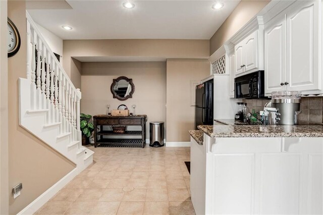 kitchen featuring stone countertops, white cabinetry, black appliances, a peninsula, and baseboards