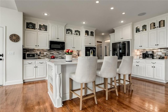 kitchen featuring a kitchen island with sink, white cabinets, and black appliances