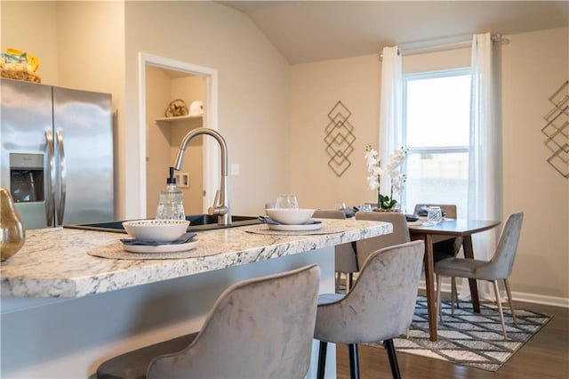 kitchen with baseboards, stainless steel fridge with ice dispenser, lofted ceiling, dark wood-style flooring, and a kitchen bar