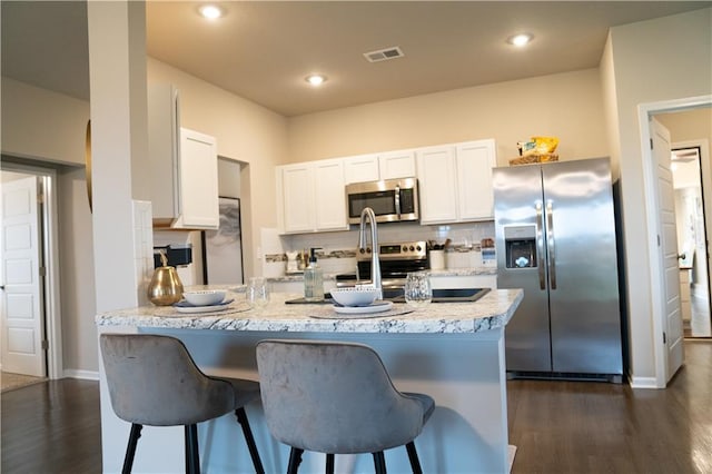 kitchen with a peninsula, appliances with stainless steel finishes, visible vents, and a kitchen breakfast bar