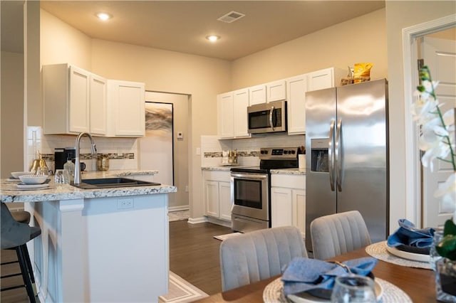 kitchen featuring visible vents, dark wood finished floors, appliances with stainless steel finishes, a peninsula, and a sink