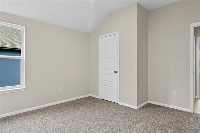 spare room featuring lofted ceiling, carpet, and baseboards