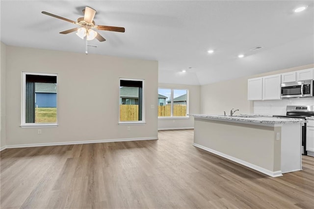 kitchen featuring stainless steel appliances, light wood-style flooring, open floor plan, a kitchen island with sink, and white cabinetry