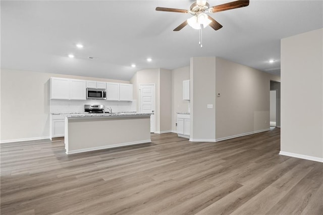 kitchen with stainless steel appliances, light wood-style floors, open floor plan, a kitchen island with sink, and white cabinetry